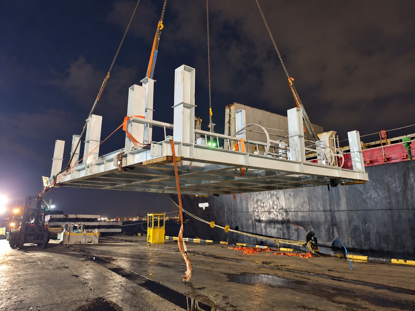 Large industrial structure being lifted beside a vessel during night-time project cargo operations